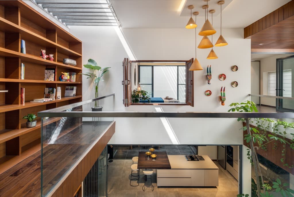 Double-height central volume with bespoke full-height teak bookcase, sculptural pendant luminaires, and kitchen island