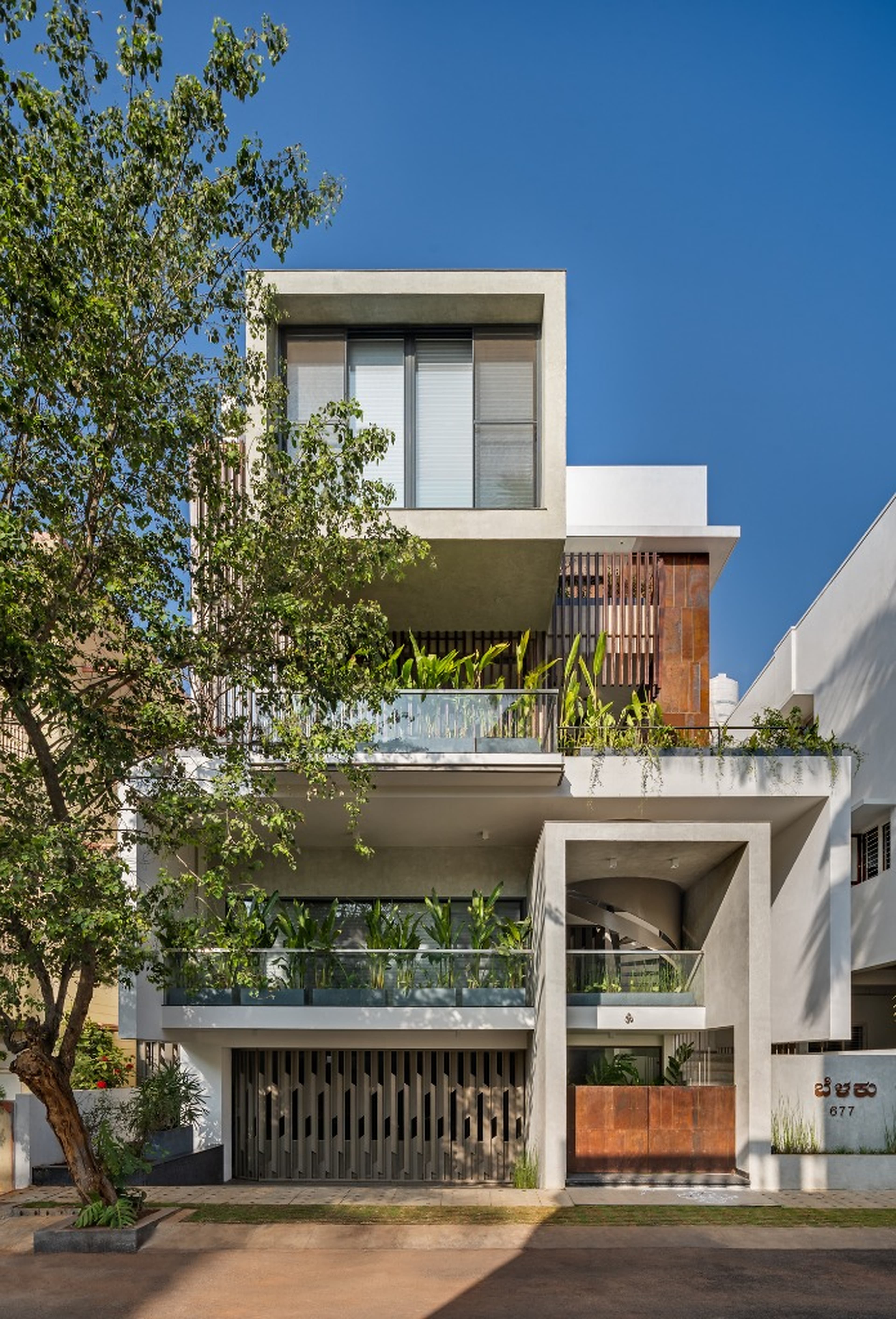Direct frontal facade highlighting stacked cubic geometries, louvers, and cascading greenery