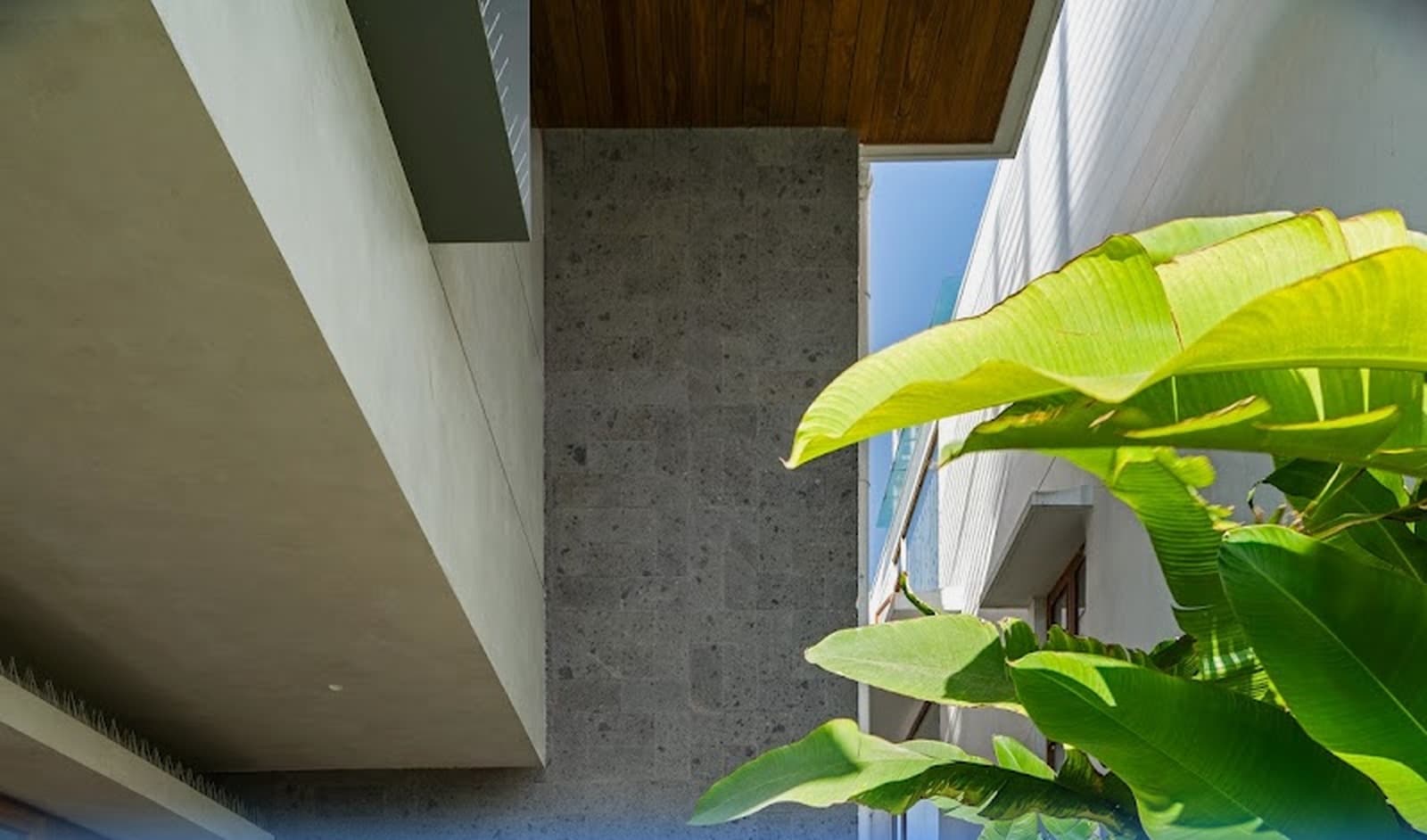 Courtyard composition highlighting coursed granite masonry, raw concrete soffits, and tropical broadleaf landscaping