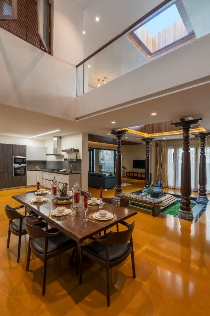 Two-story skylit central atrium linking upper walkway to the carved timber pillars and dining table below