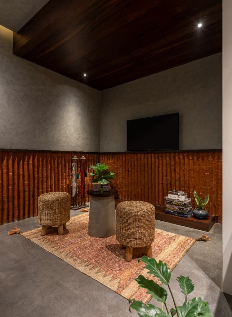 Cozy bedroom entertainment nook with wall-mounted media display, woven rattan poufs, and fluted terracotta acoustic wall