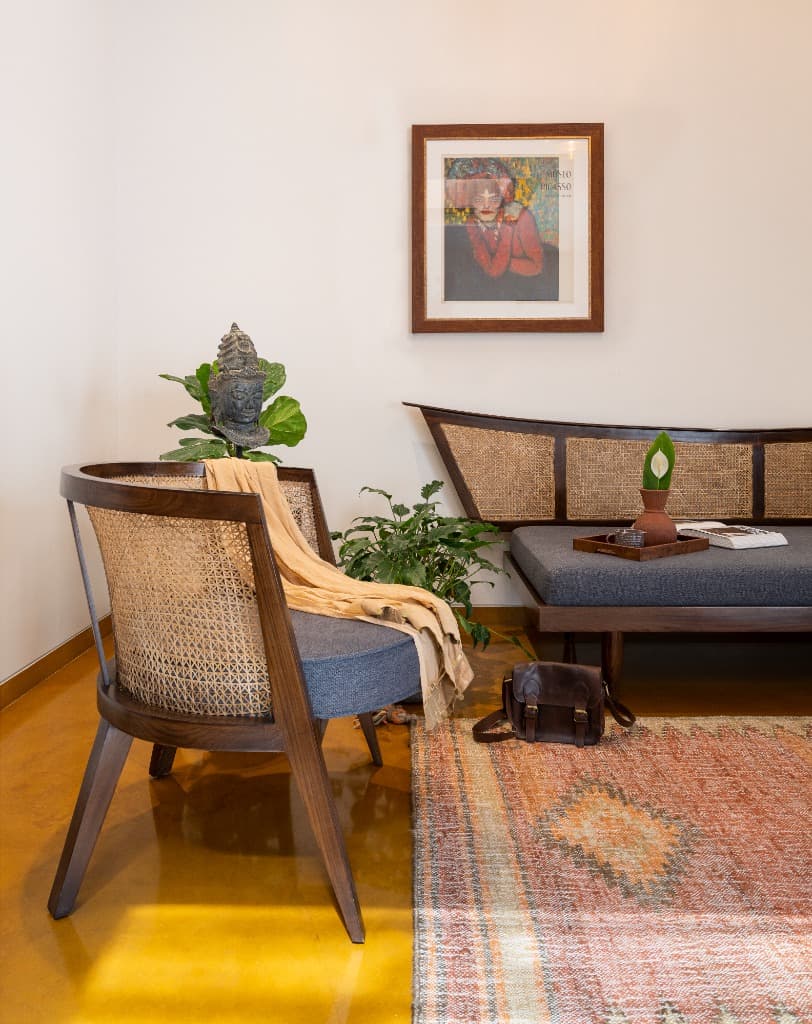 Intimate reading salon featuring curved cane armchair, artisanal daybed, and colorful kilim runner over ochre floors