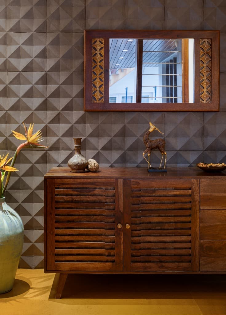 Solid teak credenza and carved mirror against geometric relief-tile feature wall with bronze gazelle accent