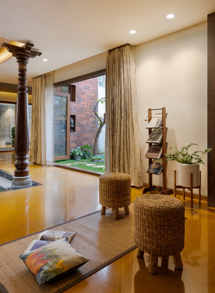 Courtyard verandah with woven rattan stools, jute rug, and floor-to-ceiling glass door opening to the brick-walled garden