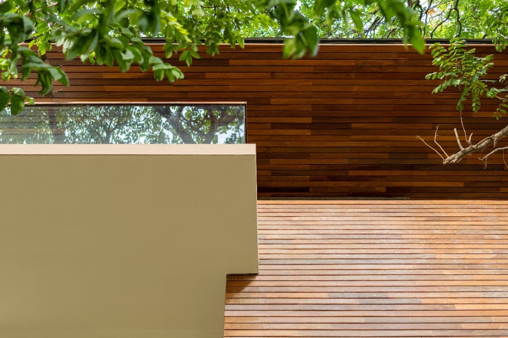 Close-up of horizontal timber soffit and brick jali screen under the canopy of centenary trees
