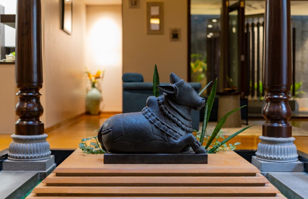 Hand-carved black stone Nandi sculpture resting on tiered terracotta pedestal between Chettinad timber pillars