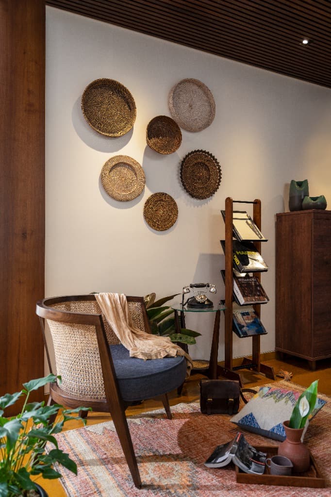 Artisanal reading nook with cane tub chair, vintage telephone side table, teak magazine stand, and woven grass wall discs