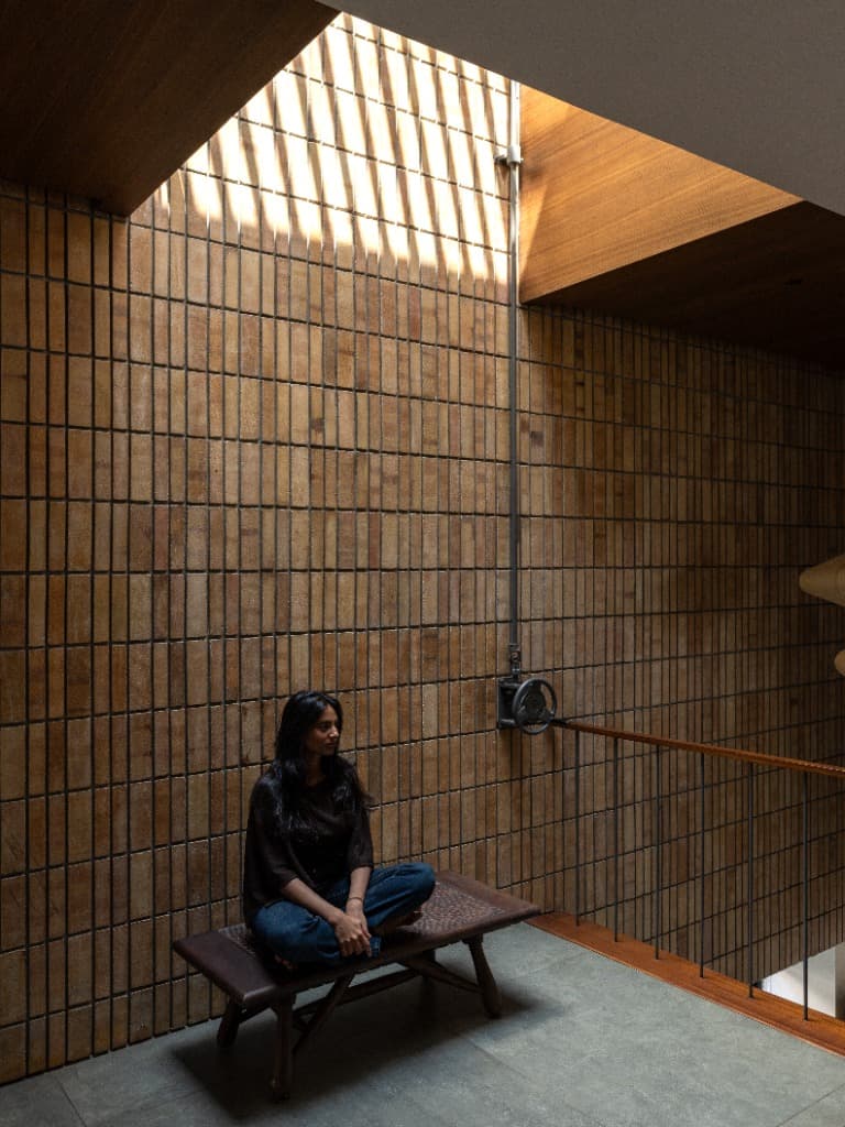 Resident sitting on woven timber bench against vertical buff brick feature wall under kinetic linear skylight shadows