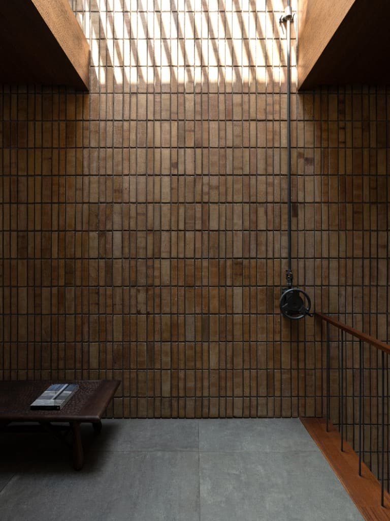 Architectural vignette of the buff brick lightwell wall, artisanal bench with design monographs, and industrial gear wheel operator