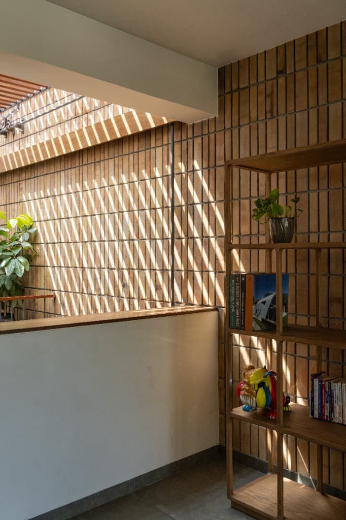Bespoke open teak shelving unit displaying books and pop art bulldog sculpture against diagonal pergola sun shadows