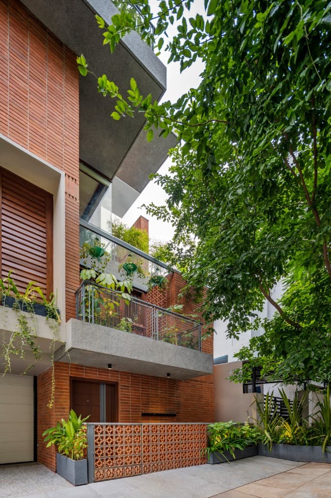 Daylight street perspective framed by surrounding tree foliage, showcasing cantilevered concrete canopies and wire-cut brickwork