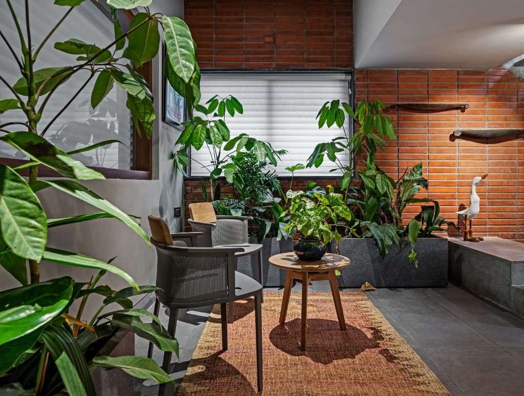 Intimate garden sitting area with contemporary woven armchairs, tribal kilim rug, and lush indoor tropical foliage against brickwork