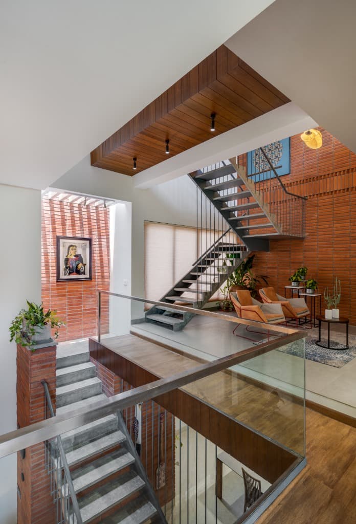 Multi-level spatial dialogue connecting the glass-railed bridge, intermediate stair flight, and brick-clad lightwell
