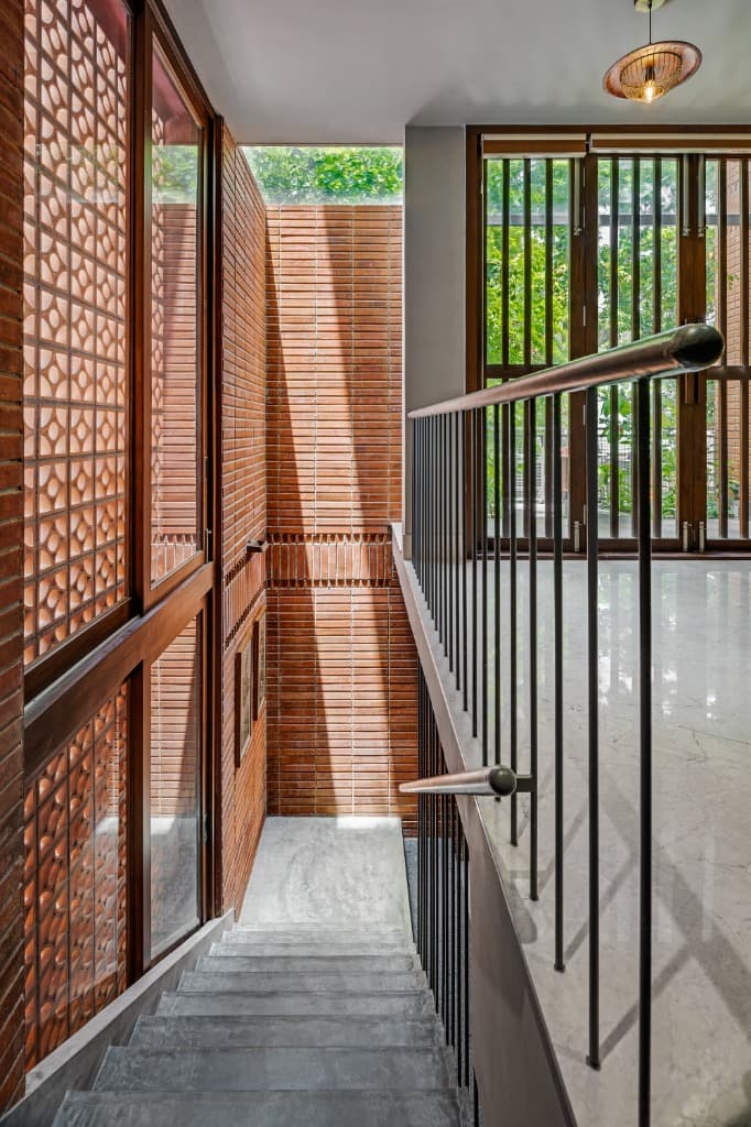 Mezzanine corridor overlooking the skylit stairwell with full-height terracotta jali wall and timber balcony doors