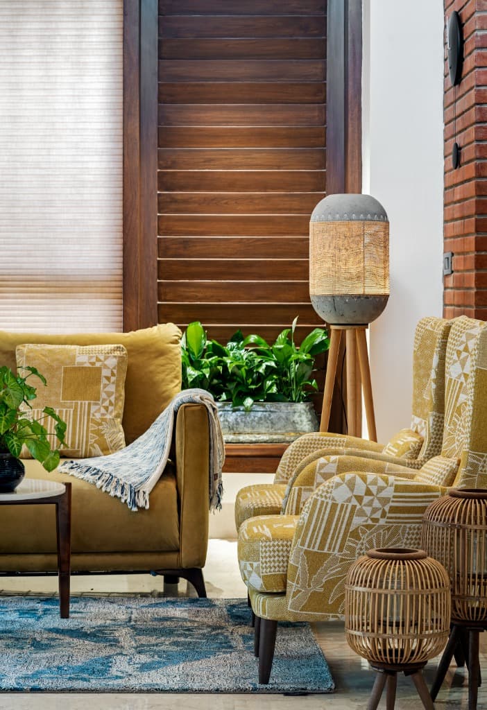 Living room reading corner with patterned mustard armchairs, artisanal concrete and woven tripod lamp, and timber louvers