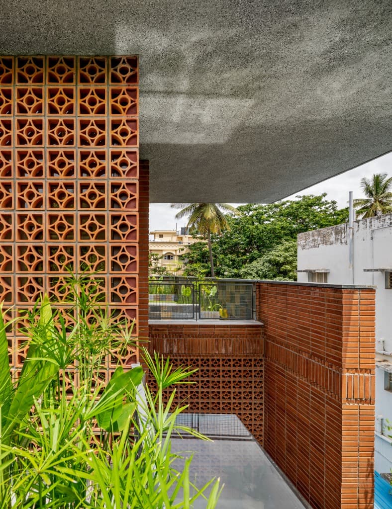 Architectural material junction showing the intricate terracotta breeze blocks, wire-cut brick parapet, and deep cantilevered concrete roof canopy