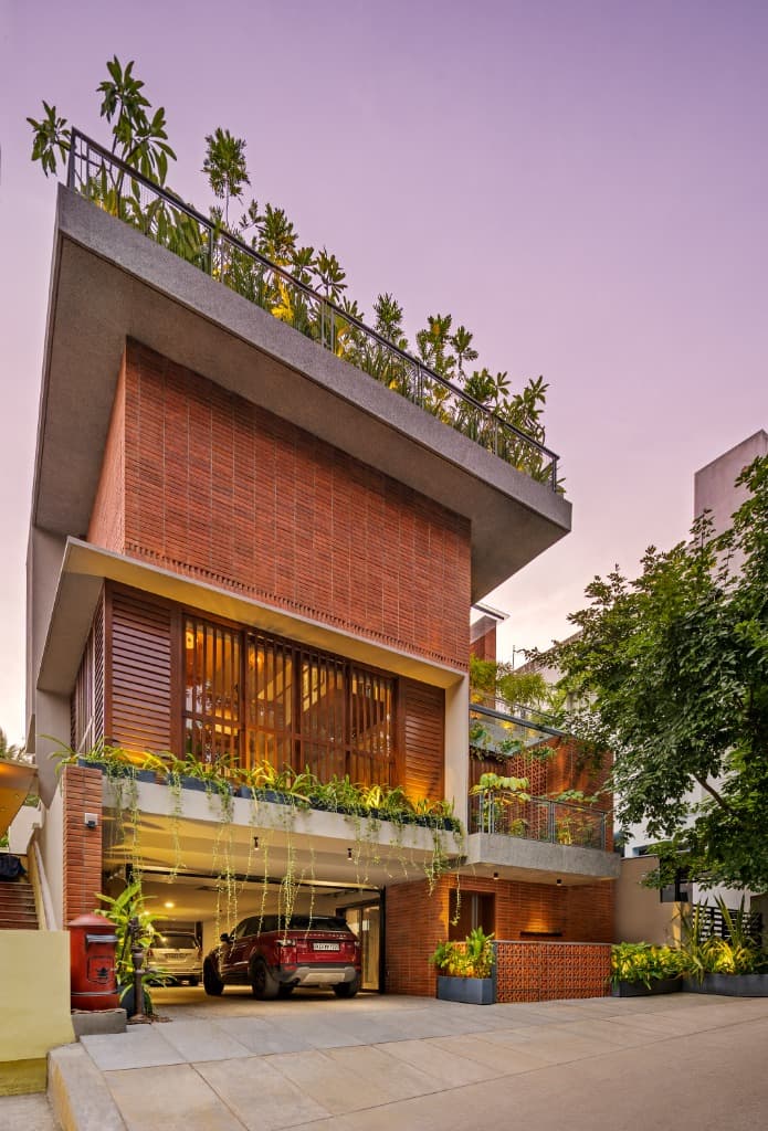 Dramatic low-angle dusk view showing layered cantilevered slabs, timber bay louvers, and warm architectural lighting