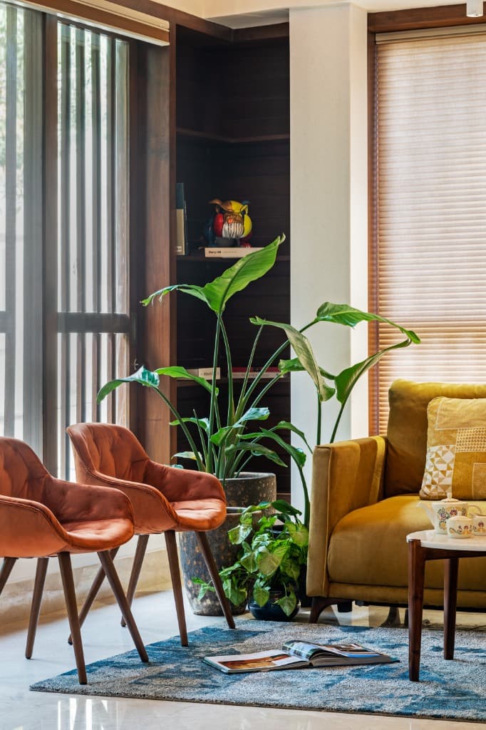Intimate lounge nook featuring rust velvet armchairs, lush bird of paradise foliage, blue rug, and bespoke timber window slats