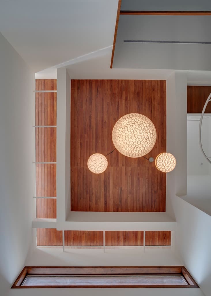 Direct upward perspective of the skylit timber ceiling featuring bespoke circular textured luminous pendant fixtures