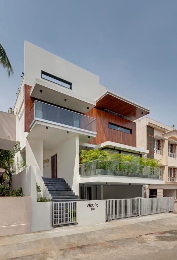 Crisp daylight street perspective showing the contrasting dialogue between white stucco frames, teak cladding, and green palms