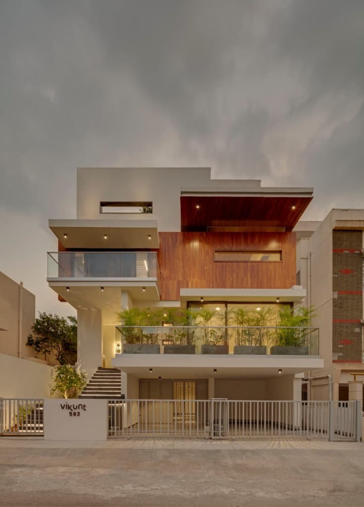 Twilight elevation under atmospheric overcast skies showcasing cantilevered teak volumes, illuminated stair, and planter balconies