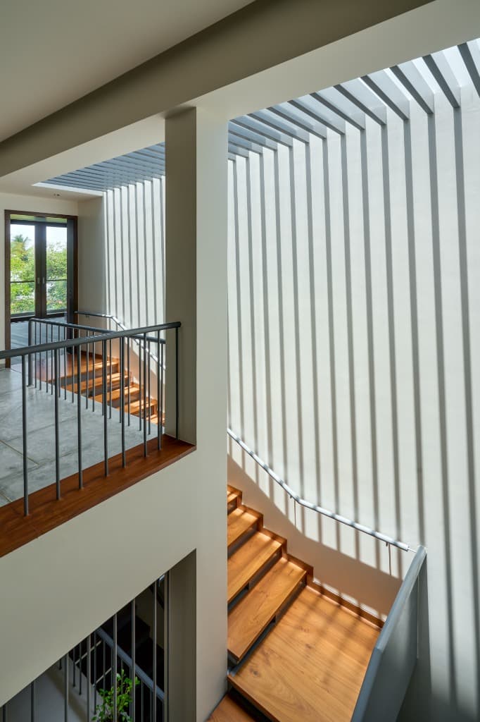 Upper stairwell illuminated by linear slatted pergola skylight casting rhythmic geometric shadow patterns